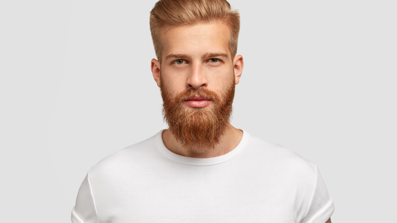 Headshot of red haired serious young male blogger looks confidently at camera, thinks about new content of his web page, dressed casually, earns money distantly, isolated over white background